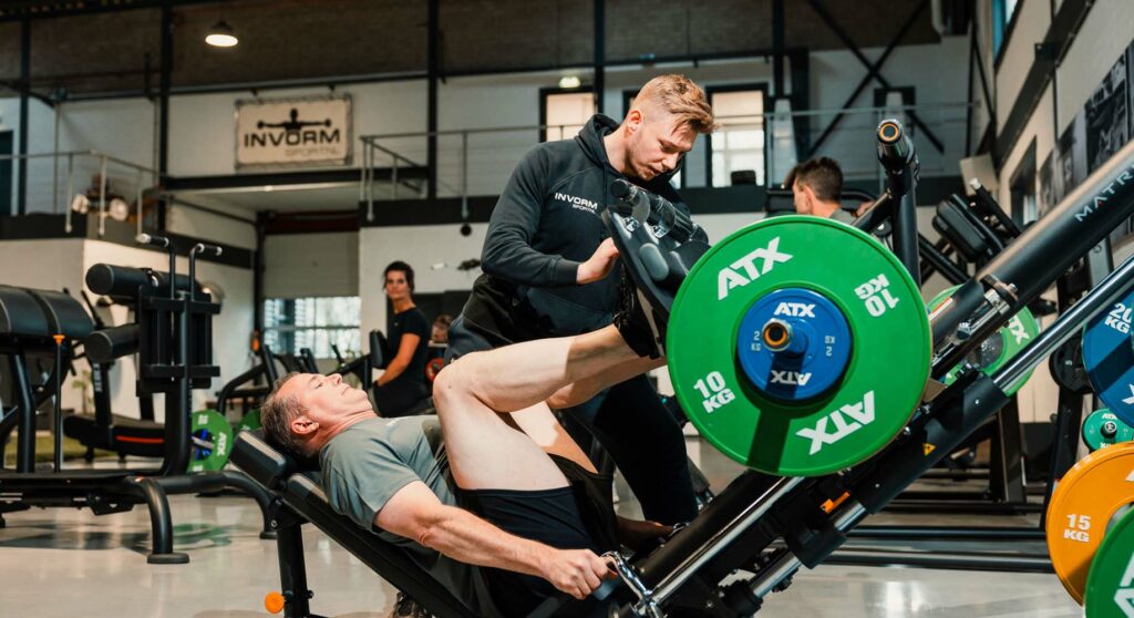 personal trainer en man die legpress doet